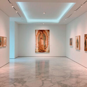 Cuadro de la Virgen de Guadalupe tamaño original expuesto en galería de arte contemporáneo con piso de mármol y muros blancos.